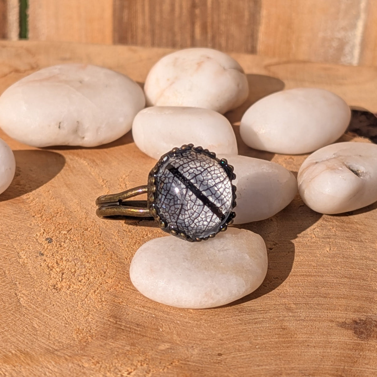 Angled view of a Midnight Lace black leaf resin ring among white stones, showing its rustic brown split band, EL-Creations