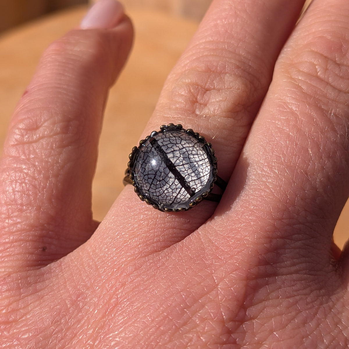 Close-up of a Midnight Lace botanical resin ring worn on a finger in sunlight, showing its lace-like black leaf pattern, EL-Creations