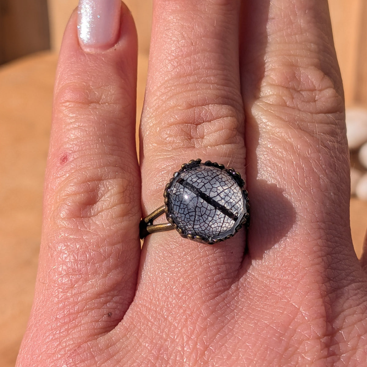 Front view of an adjustable black leaf resin ring worn on an outstretched hand, showing its round botanical centre and brown band, EL-Creations
