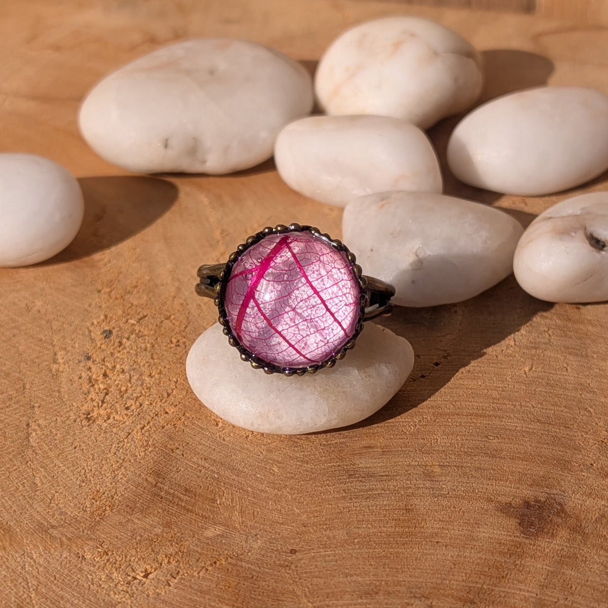 Fuchsia Lace pink leaf resin ring balanced on a white pebble among smooth stones on sunlit wood, EL-Creations
