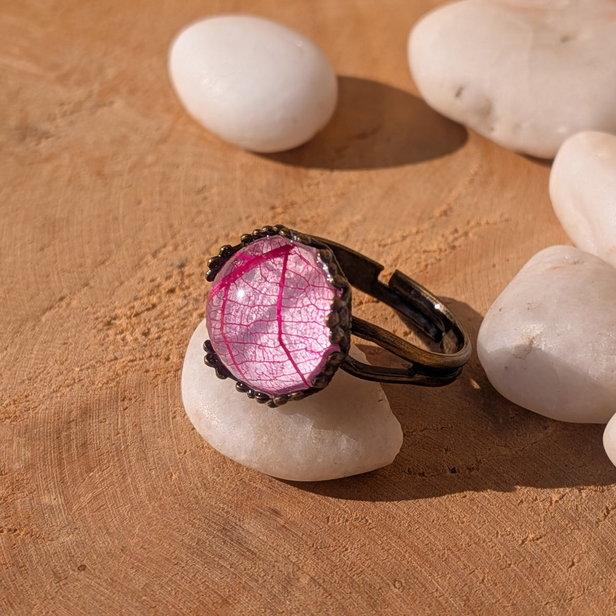 Side view of a Fuchsia Lace resin ring resting on a white stone, showing the open adjustable band and raised pink leaf cabochon, EL-Creations
