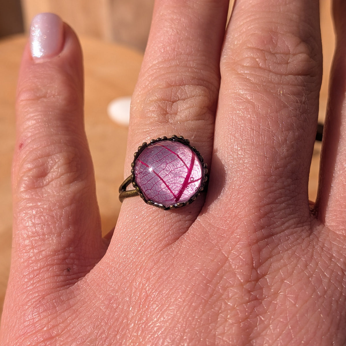 Front view of a Fuchsia Lace botanical resin ring on an outstretched hand, showing its delicate pink leaf pattern, EL-Creations