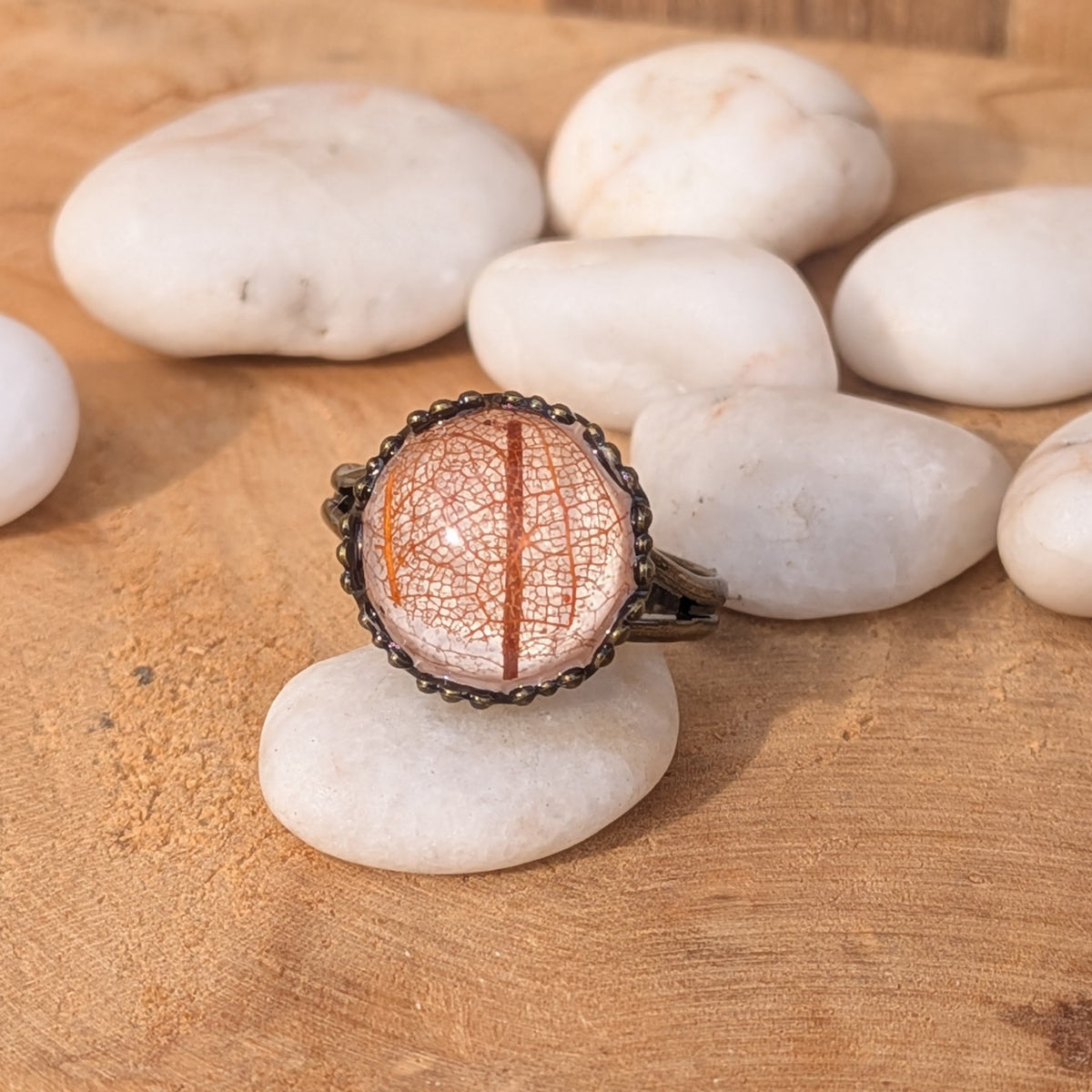 Front view of an autumn botanical resin ring on a white stone, showing a warm orange leaf stem and delicate beige veins, EL-Creations