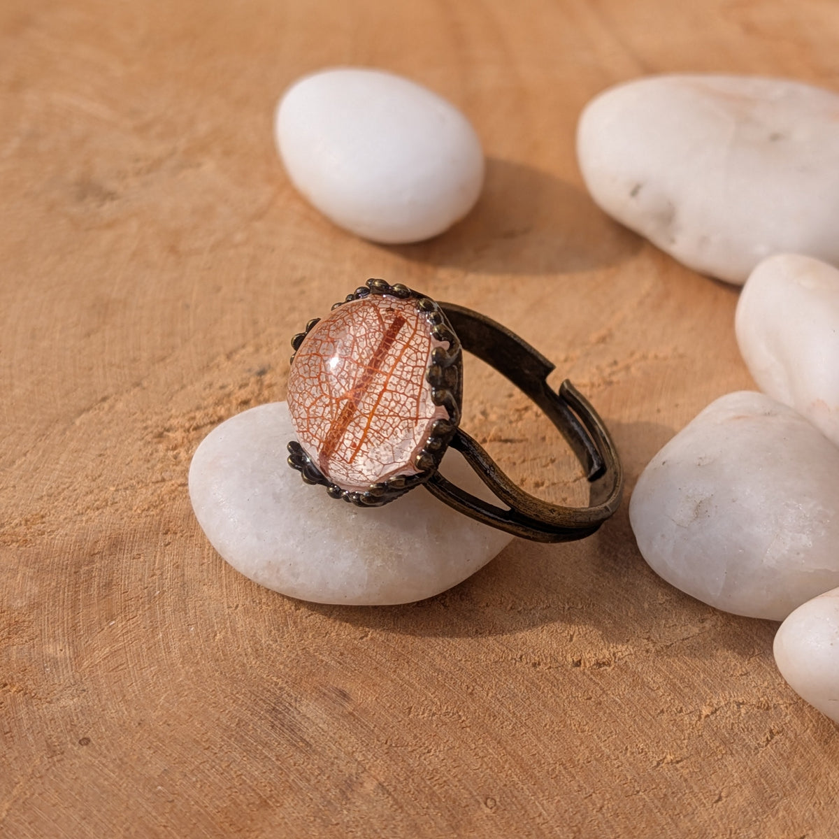Side view of an orange and beige leaf resin ring on a white pebble, showing its open adjustable brown band and raised dome, EL-Creations