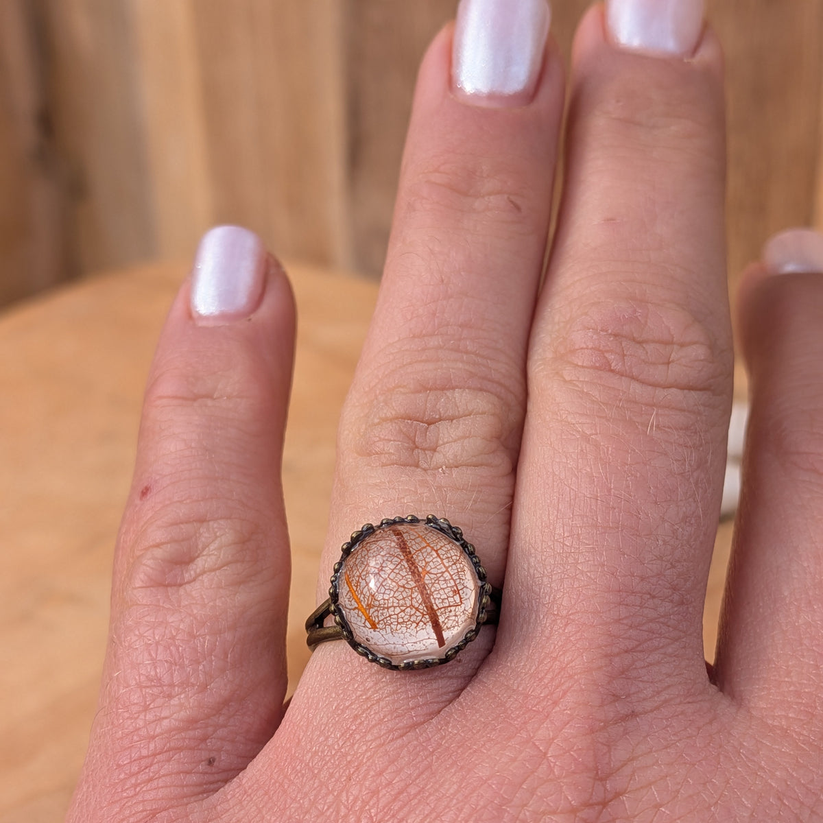 Front view of an adjustable Autumn Glow leaf resin ring worn on an outstretched hand, showing its warm botanical colours, EL-Creations