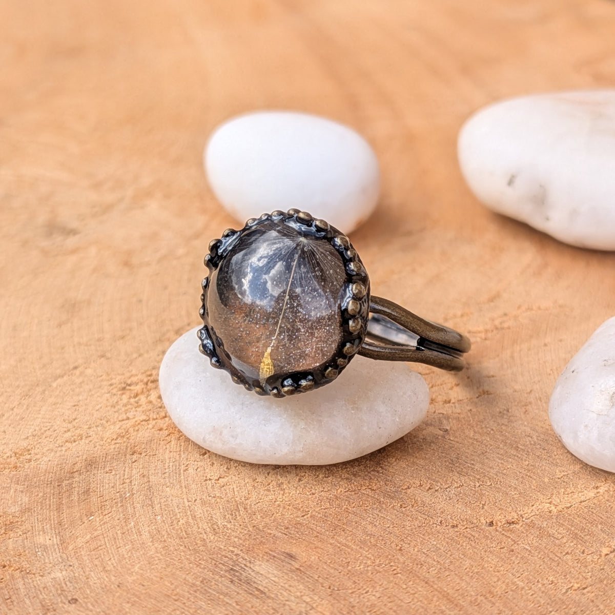 Angled view of a single dandelion seed resin ring on a white stone, showing its decorative rustic brown setting and split band, EL-Creations