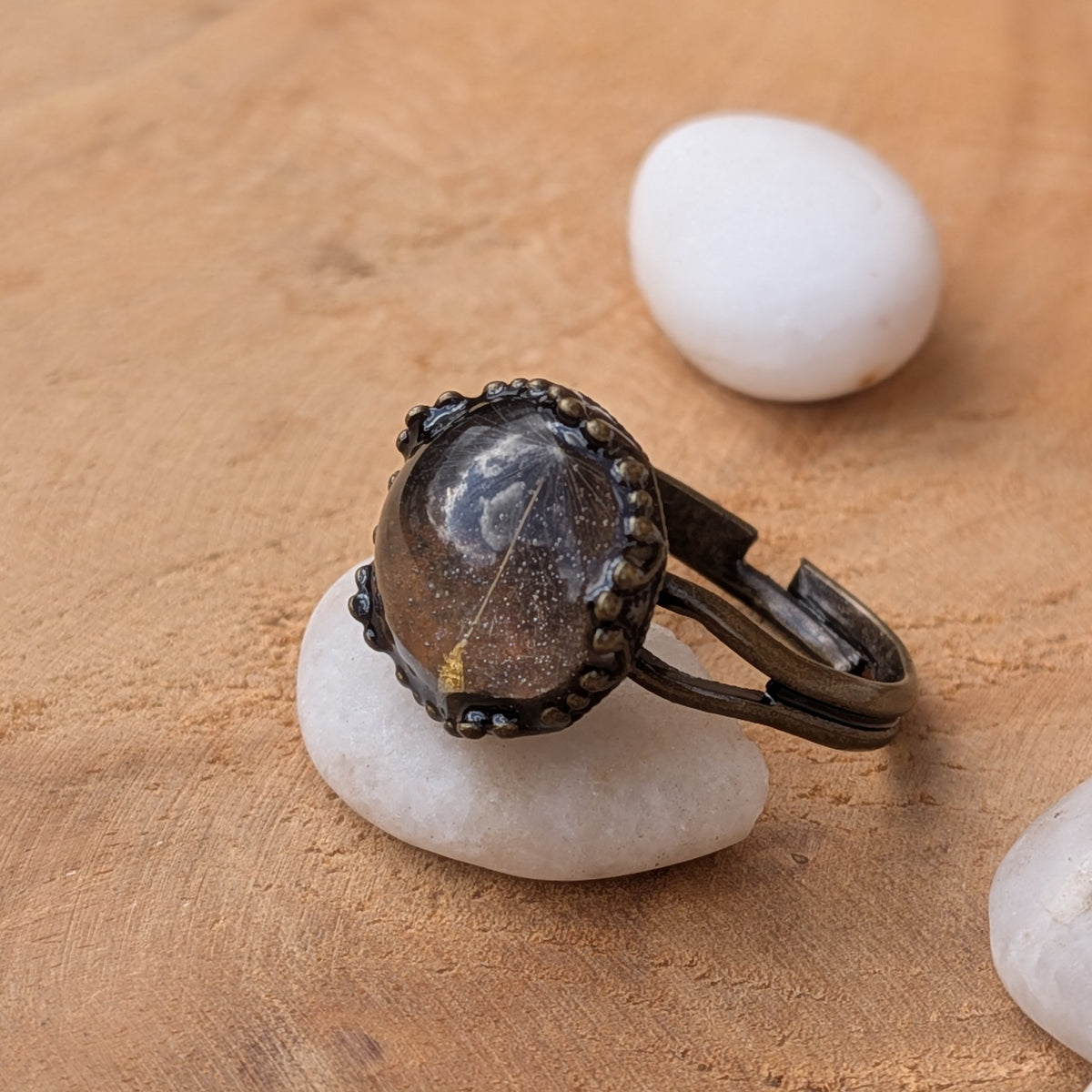 Side view of a One Little Wish dandelion resin ring on a white pebble, showing its raised cabochon and open adjustable band, EL-Creations