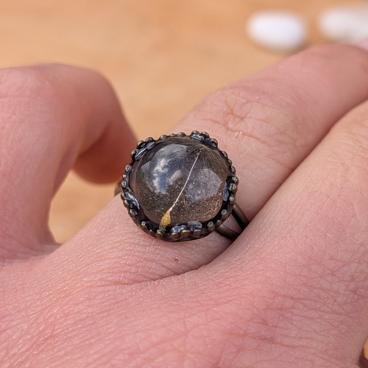 Close-up of a One Little Wish resin ring worn on a finger, highlighting the single dandelion seed beneath the glossy surface, EL-Creations