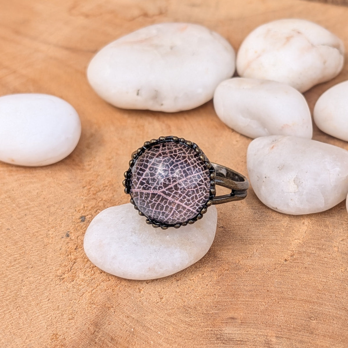 Front view of a Blush Whisper botanical resin ring balanced on a white stone, with delicate pale pink leaf veins beneath the glossy surface, EL-Creations