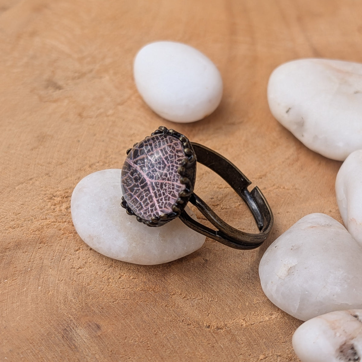 Side view of a pale pink leaf resin ring on a white pebble, showing its open adjustable brown band and raised cabochon, EL-Creations