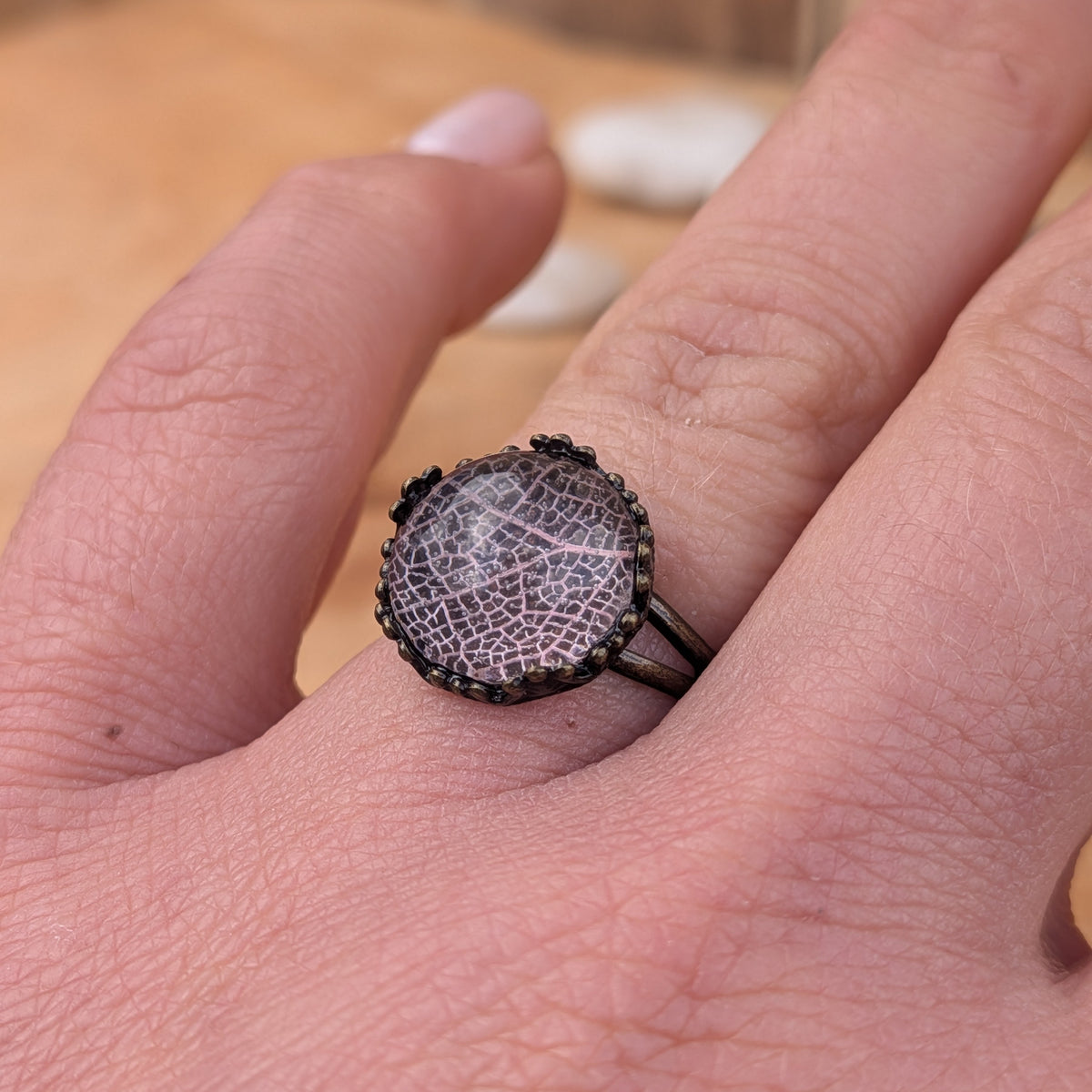 Angled view of a Blush Whisper resin ring worn on a finger, showing its delicate pale pink botanical pattern and rustic setting, EL-Creations