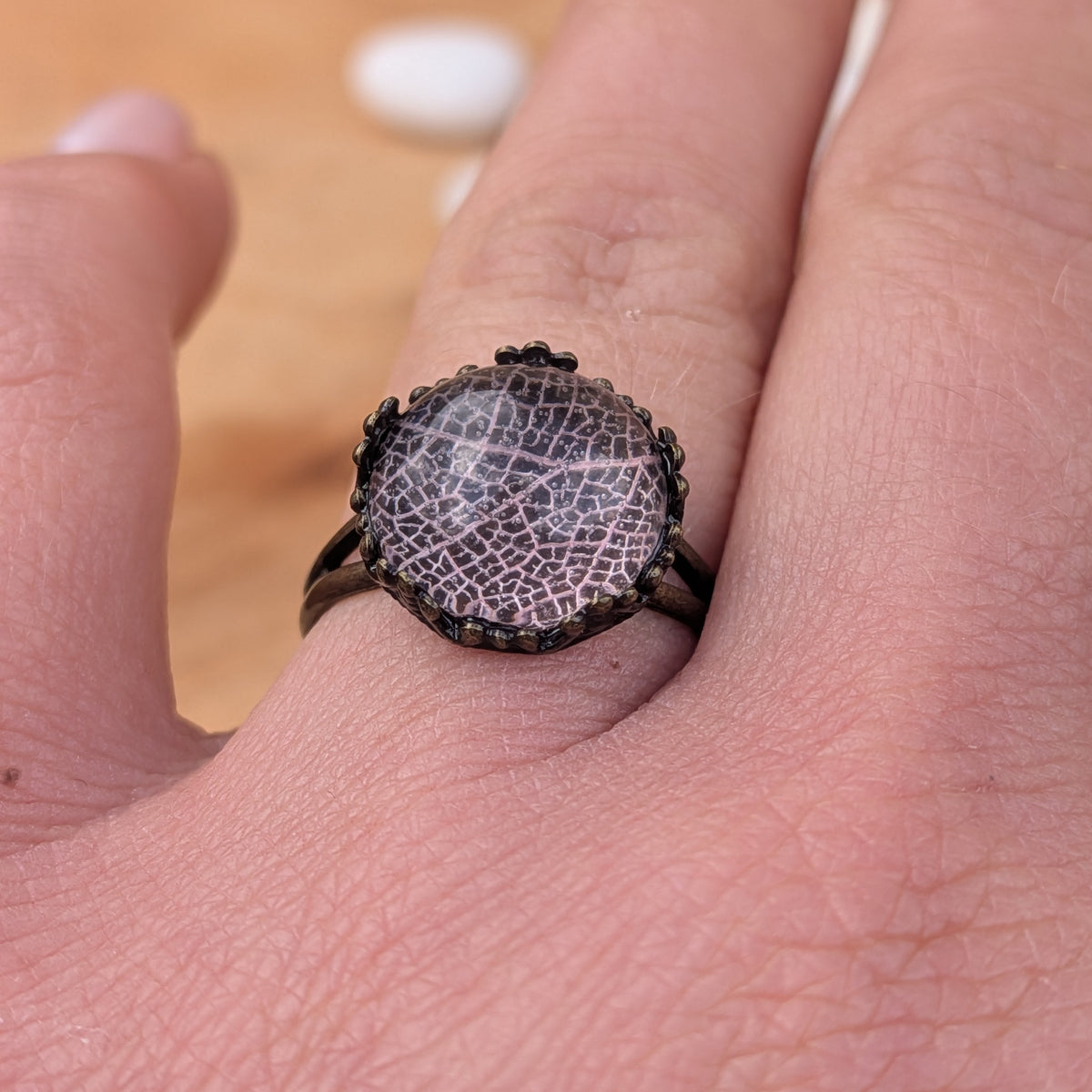 Close-up of a very pale pink skeleton leaf ring worn on a finger, highlighting the lace-like veins beneath the resin dome, EL-Creations