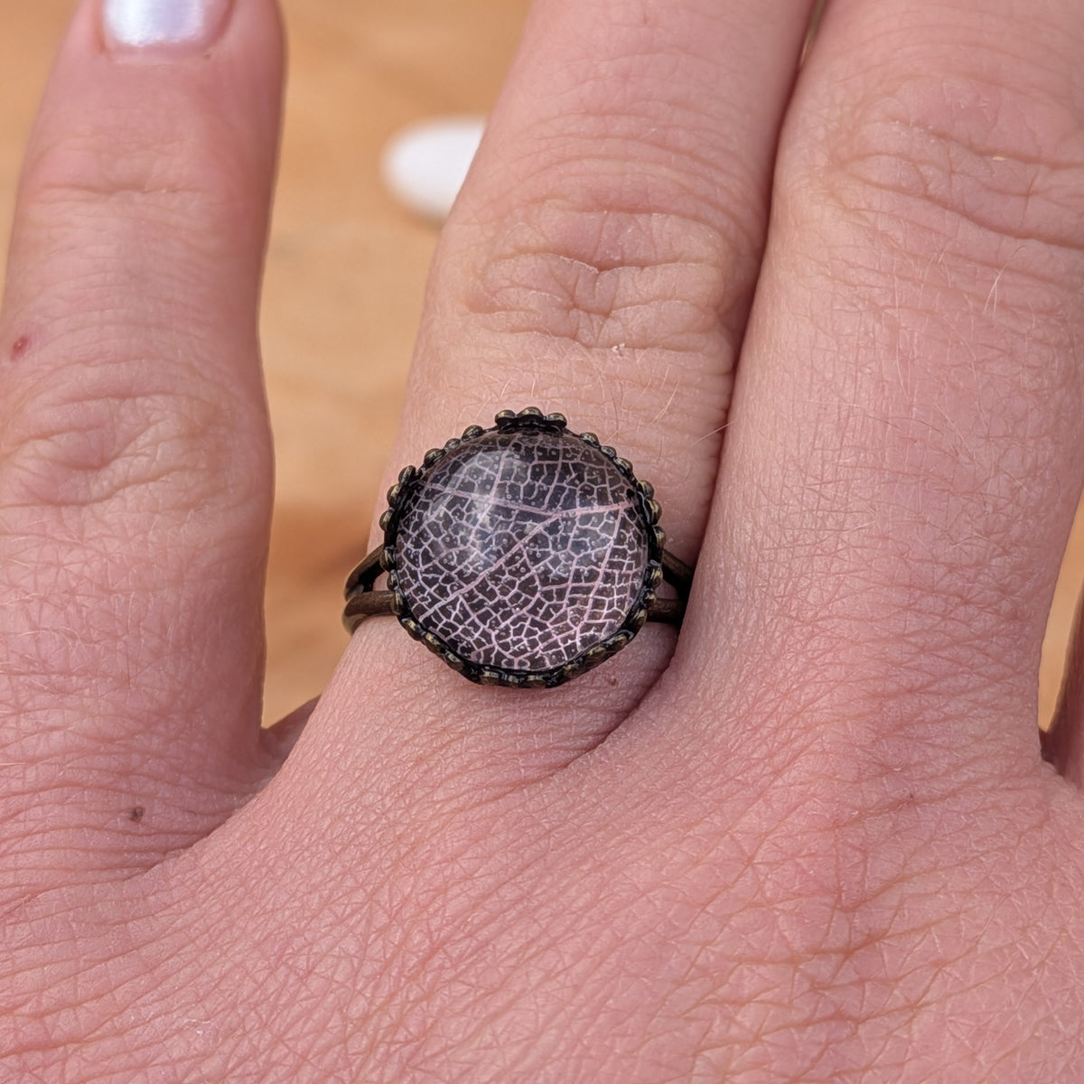 Front view of an adjustable Blush Whisper botanical resin ring worn on an outstretched hand, showing its round leaf cabochon, EL-Creations
