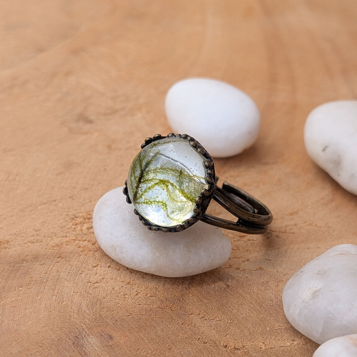 Side view of a Moss Haven botanical resin ring on a white pebble, highlighting its raised cabochon and open adjustable brown band, EL-Creations