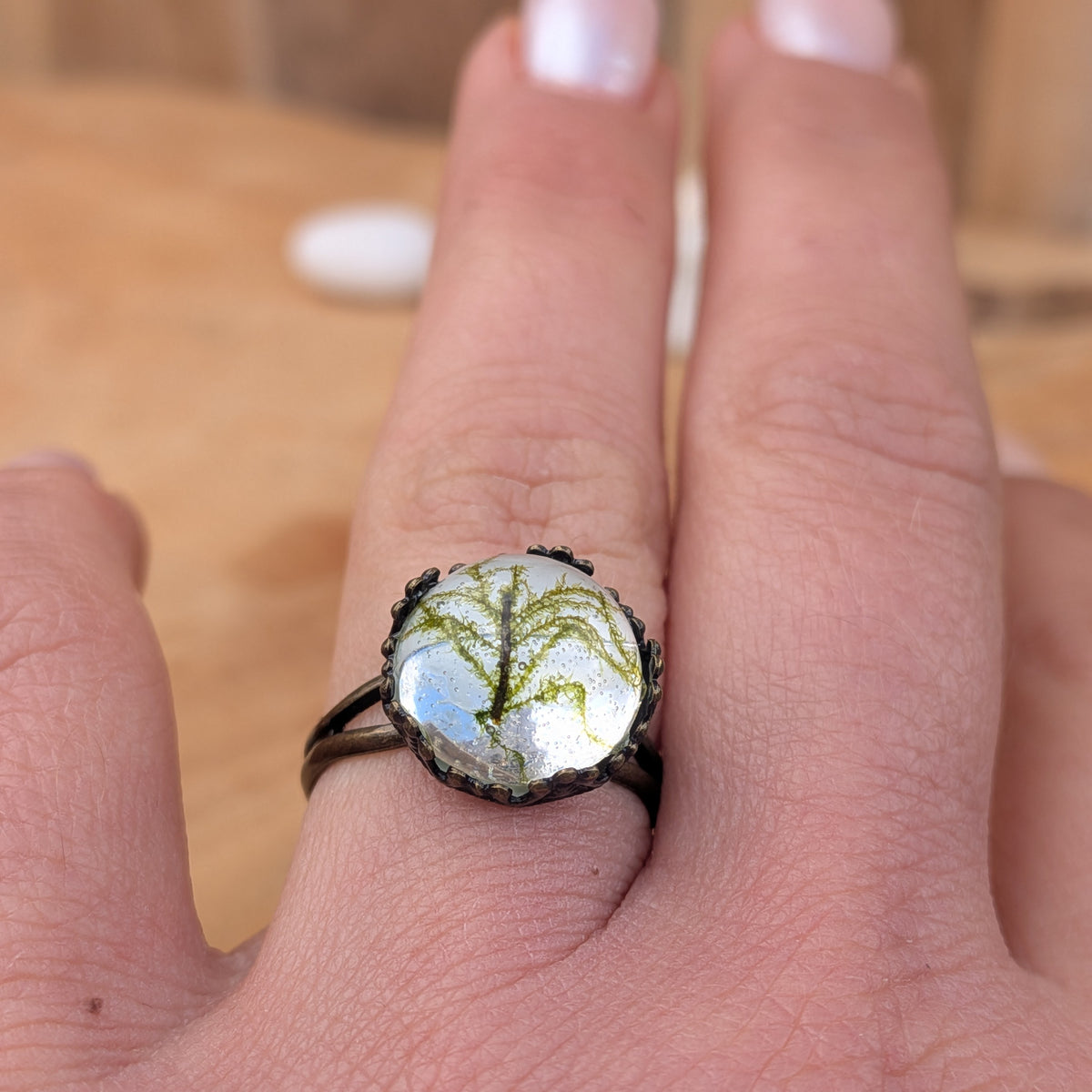 Front close-up of a real moss resin ring worn on a finger, with its rustic brown split band and delicate botanical details visible, EL-Creations