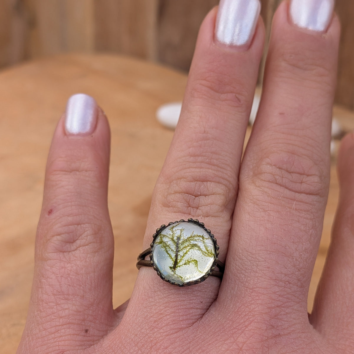 Moss Haven botanical resin ring worn on an outstretched hand, showing its round moss centre and decorative rustic brown setting, EL-Creations