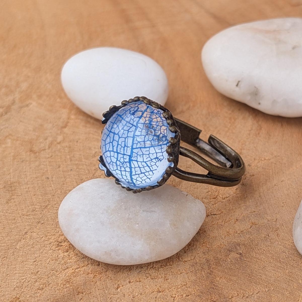 Azure Lace blue skeleton leaf resin ring on a white pebble, with its decorative rustic brown setting and split band visible, EL-Creations