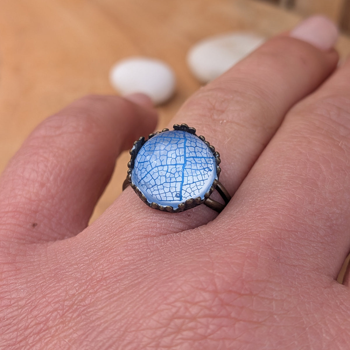 Close-up of an Azure Lace resin ring worn on a finger, showing intricate blue skeleton leaf veins beneath the glossy surface, EL-Creations