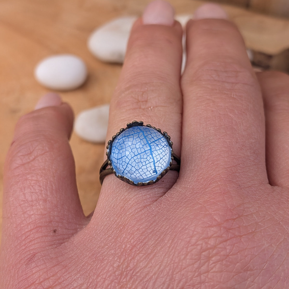 Azure Lace blue botanical resin ring worn on an outstretched hand, showing its round centre and decorative brown border, EL-Creations