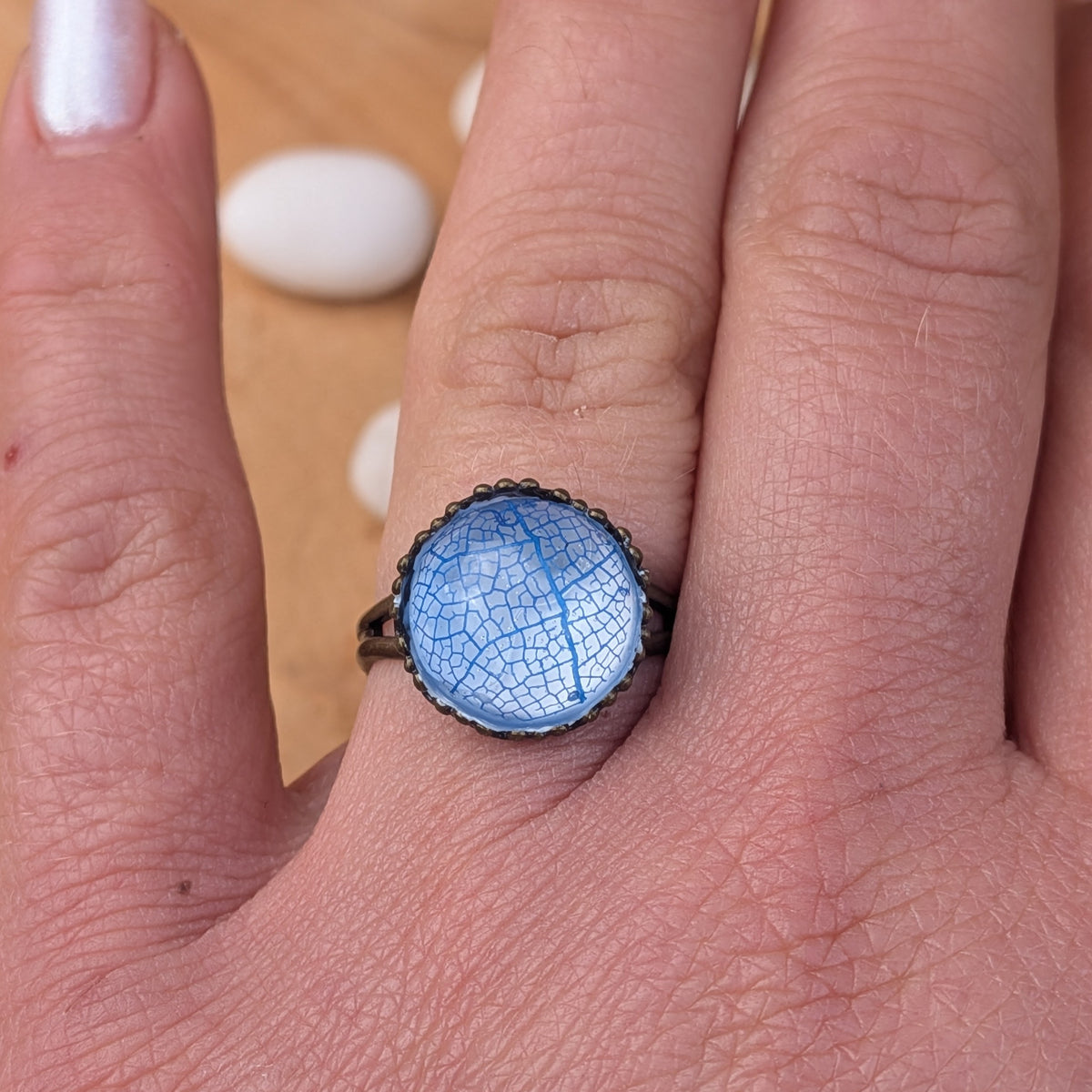 Front close-up of an adjustable blue leaf resin ring worn on a finger, highlighting its delicate vein pattern and rustic brown setting, EL-Creations