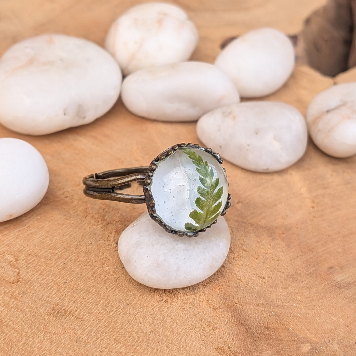 Side view of a botanical fern resin ring on a white pebble, showing its brown split band extending to the left, EL-Creations
