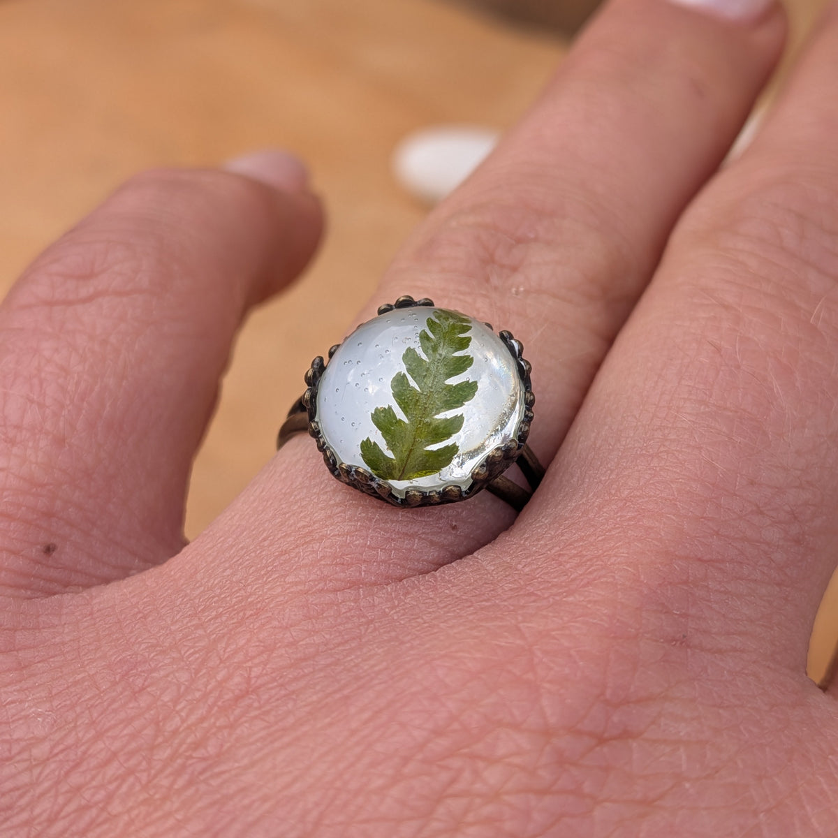 Angled view of a green fern resin ring worn on a finger, highlighting the glossy dome and delicate fern leaflets, EL-Creations