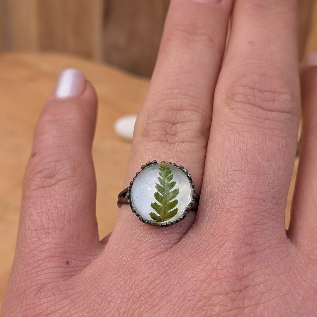 Fern Whisper botanical resin ring worn on an outstretched hand, showing its round fern centre and rustic brown band, EL-Creations