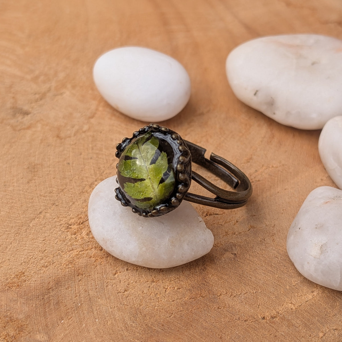 Side view of a green fern resin ring on a white stone, highlighting its open adjustable band and raised decorative setting, EL-Creations
