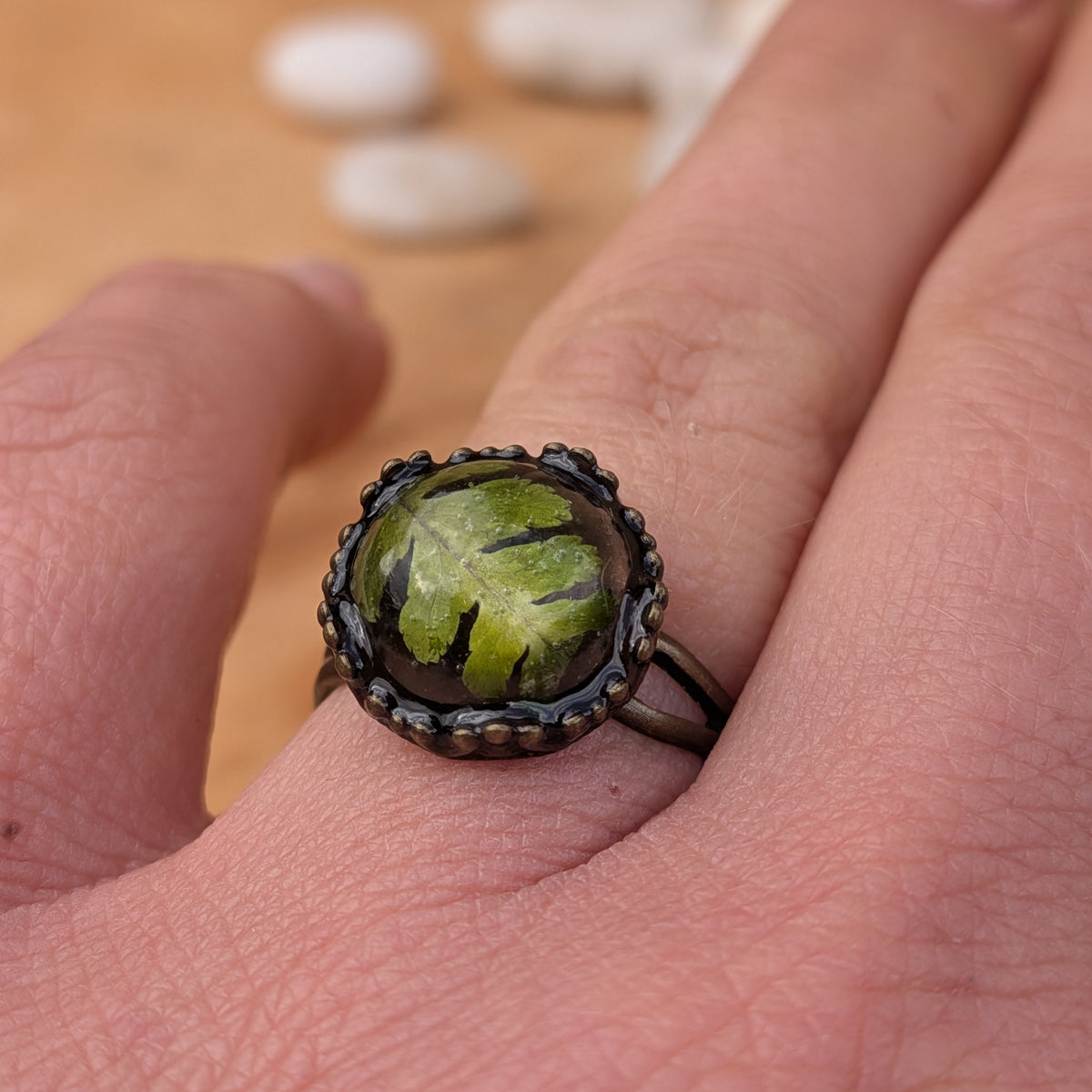 Close-up of a Woodland Fern resin ring worn on a finger, showing the textured green fern leaflets and decorative brown border, EL-Creations