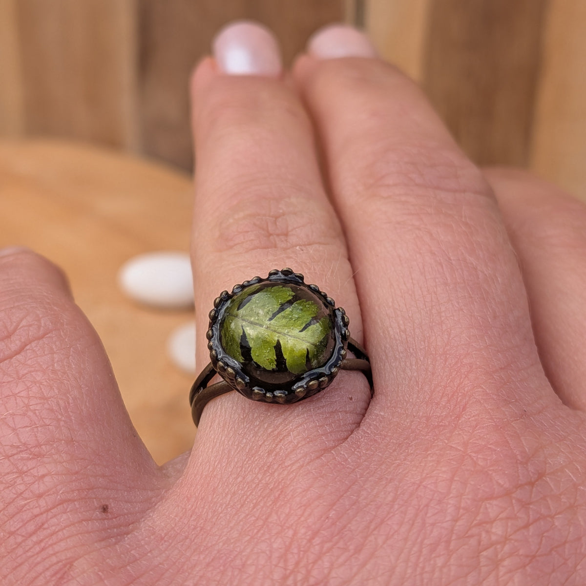 Angled view of an adjustable green fern resin ring worn on an outstretched hand, with its rustic brown split band visible, EL-Creations