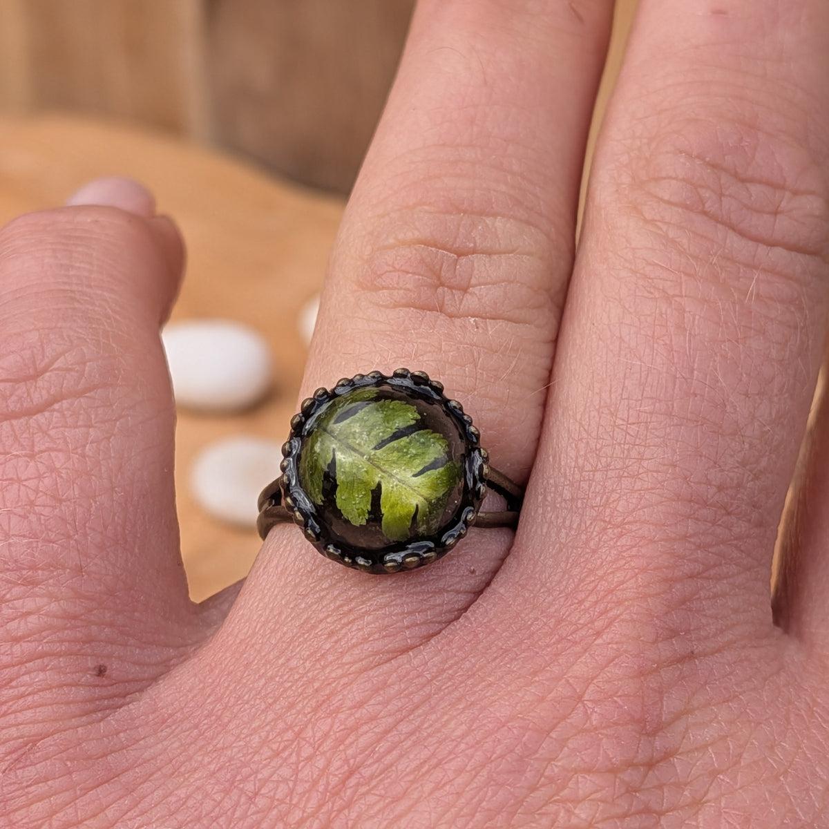 Front close-up of a Woodland Fern botanical resin ring worn on a finger, highlighting the diagonal fern arrangement beneath the domed resin, EL-Creations