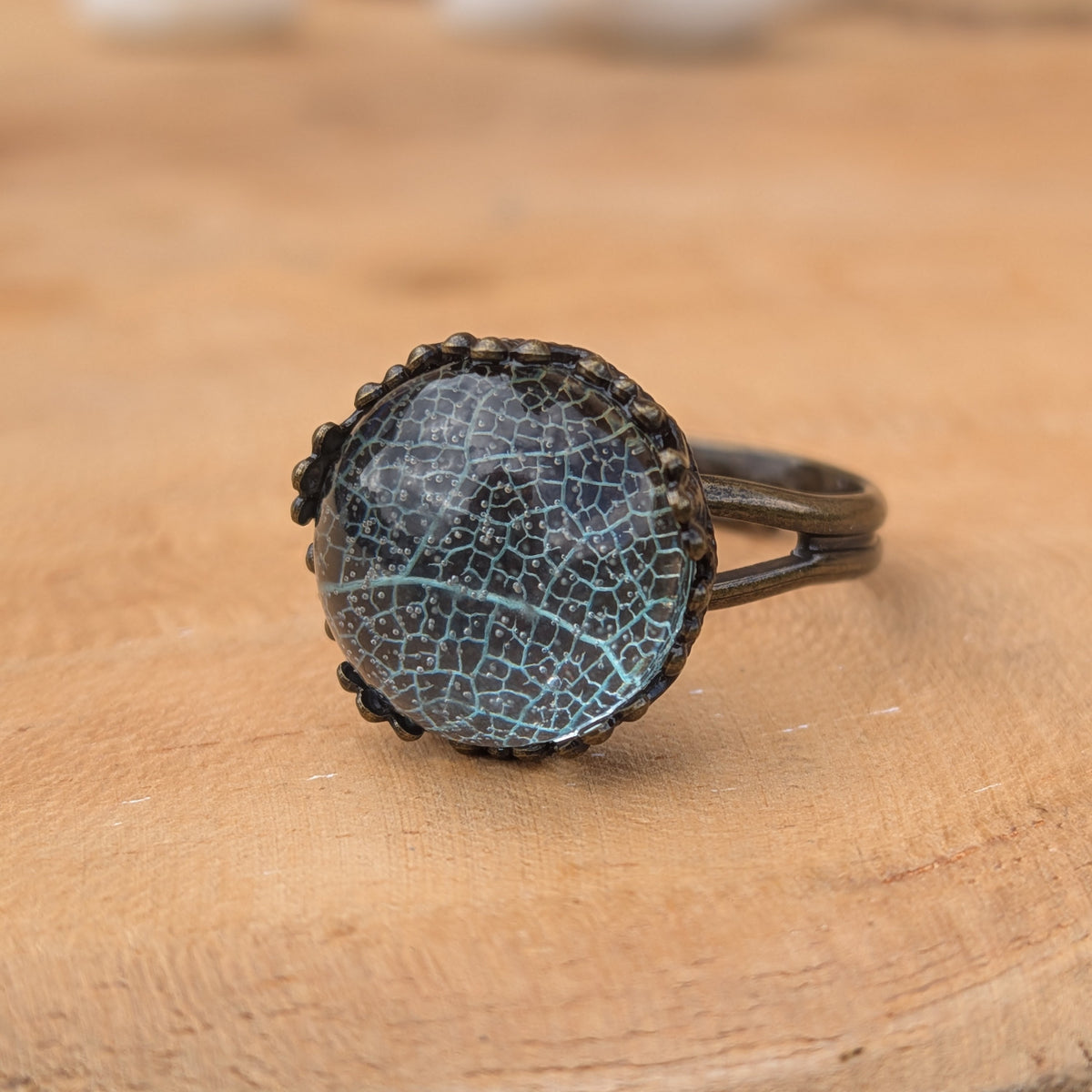 Macro view of a Seafoam Lace resin ring resting directly on wood, showing its intricate leaf pattern and rustic brown split band, EL-Creations