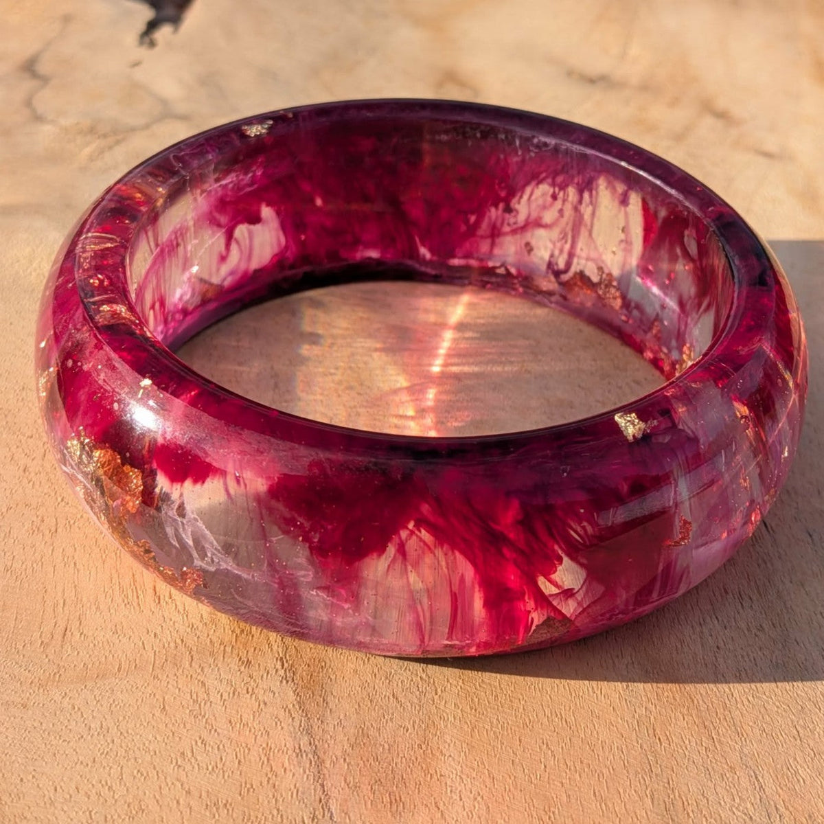 Deep red burgundy resin bangle lying flat on wooden surface showing full ring shape – EL-Creations
