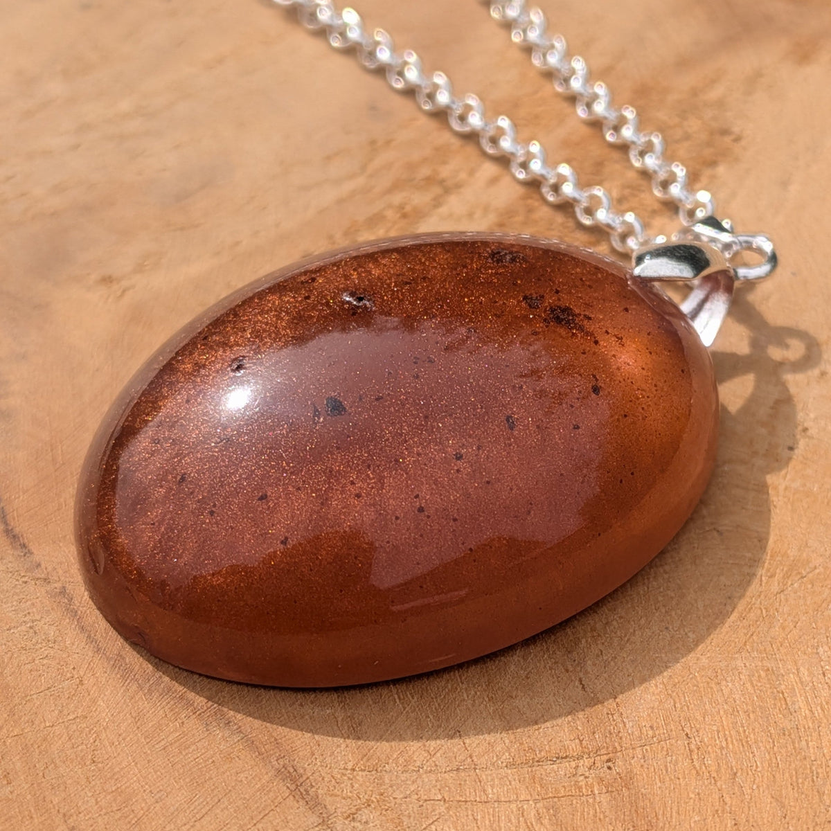 Glossy copper and bronze resin oval pendant resting on natural wood by EL-Creations