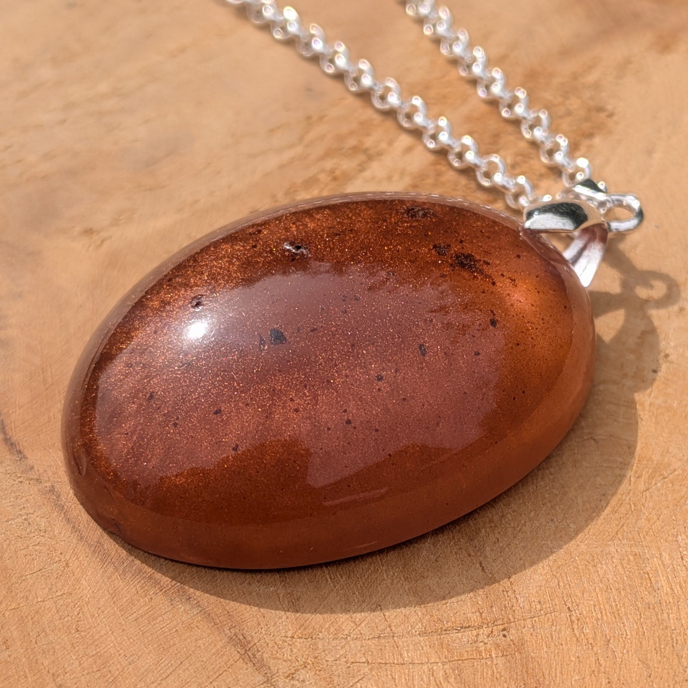 Glossy copper and bronze resin oval pendant resting on natural wood by EL-Creations