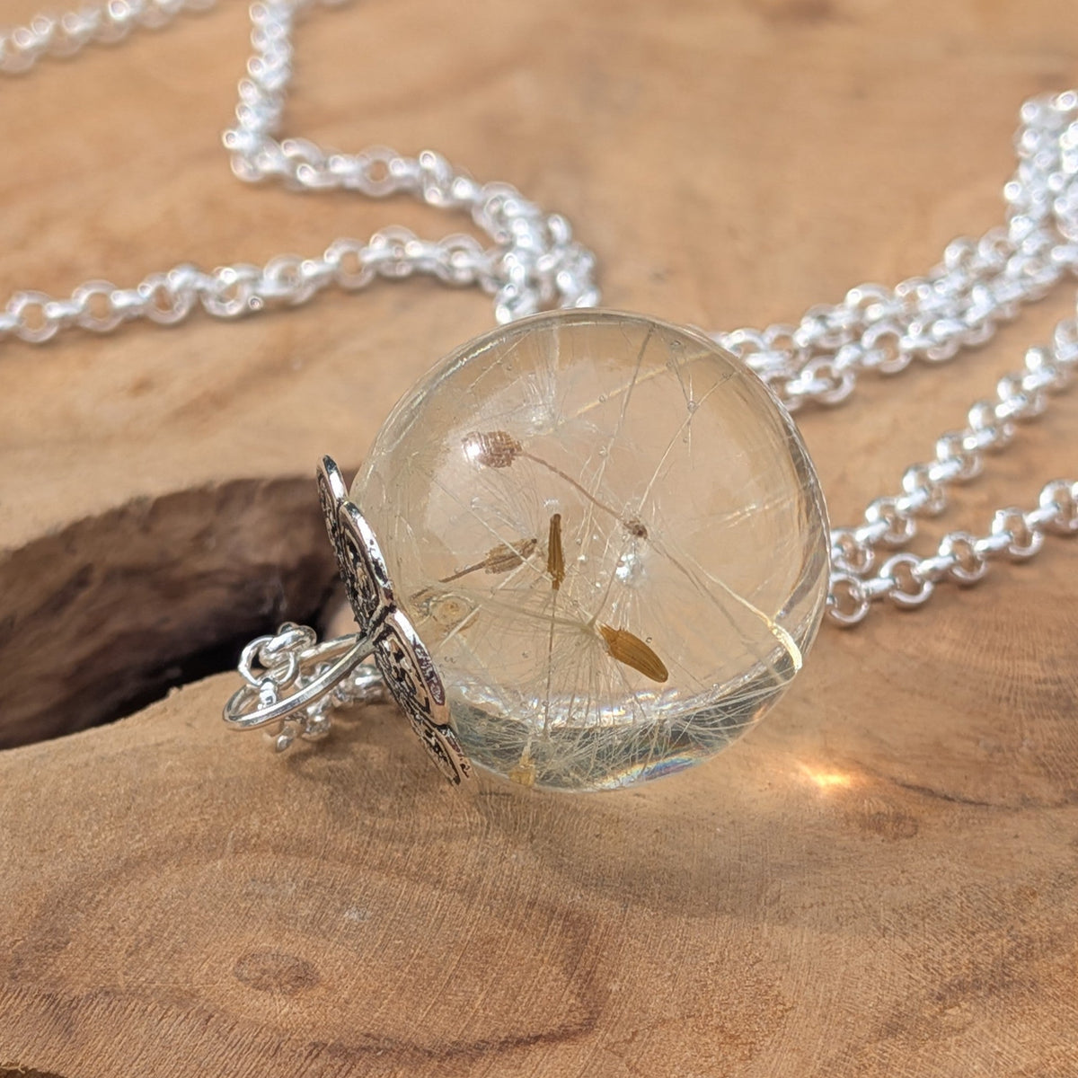 Dandelion resin globe necklace resting on natural wood by EL-Creations