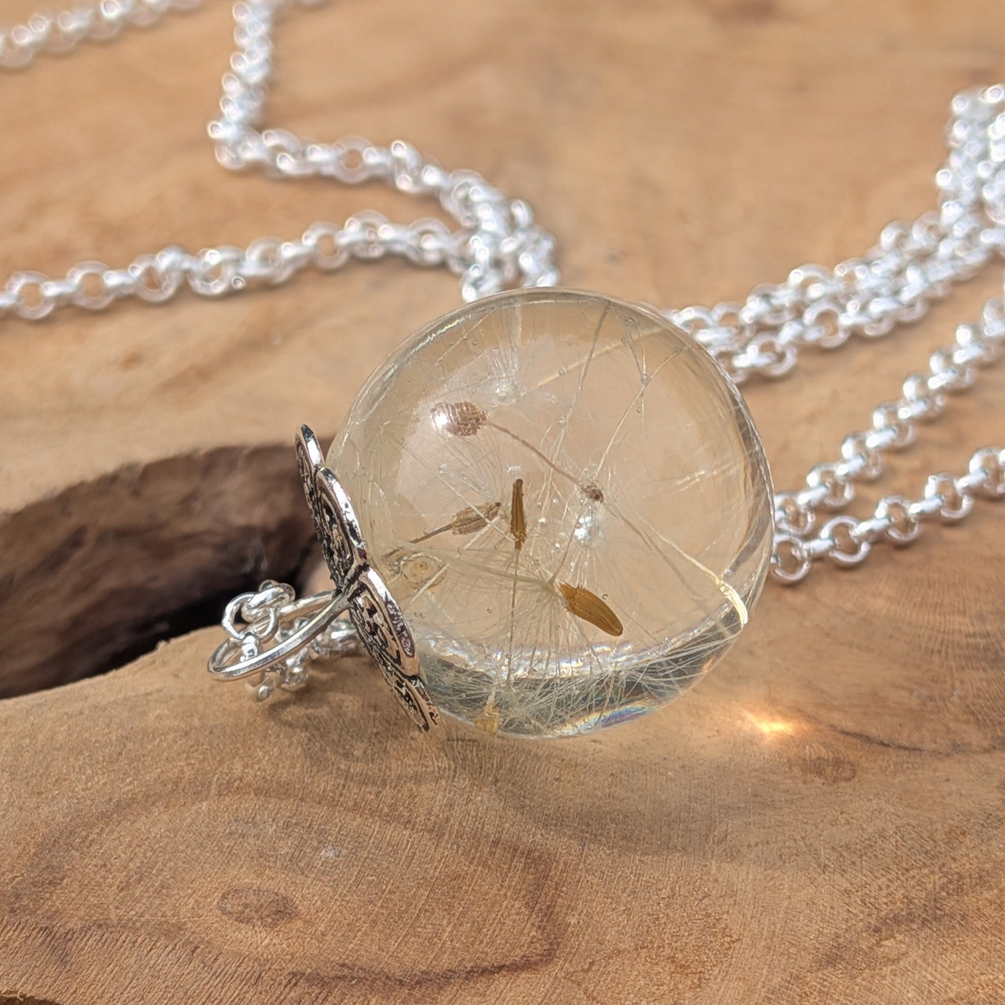 Dandelion resin globe necklace resting on natural wood by EL-Creations