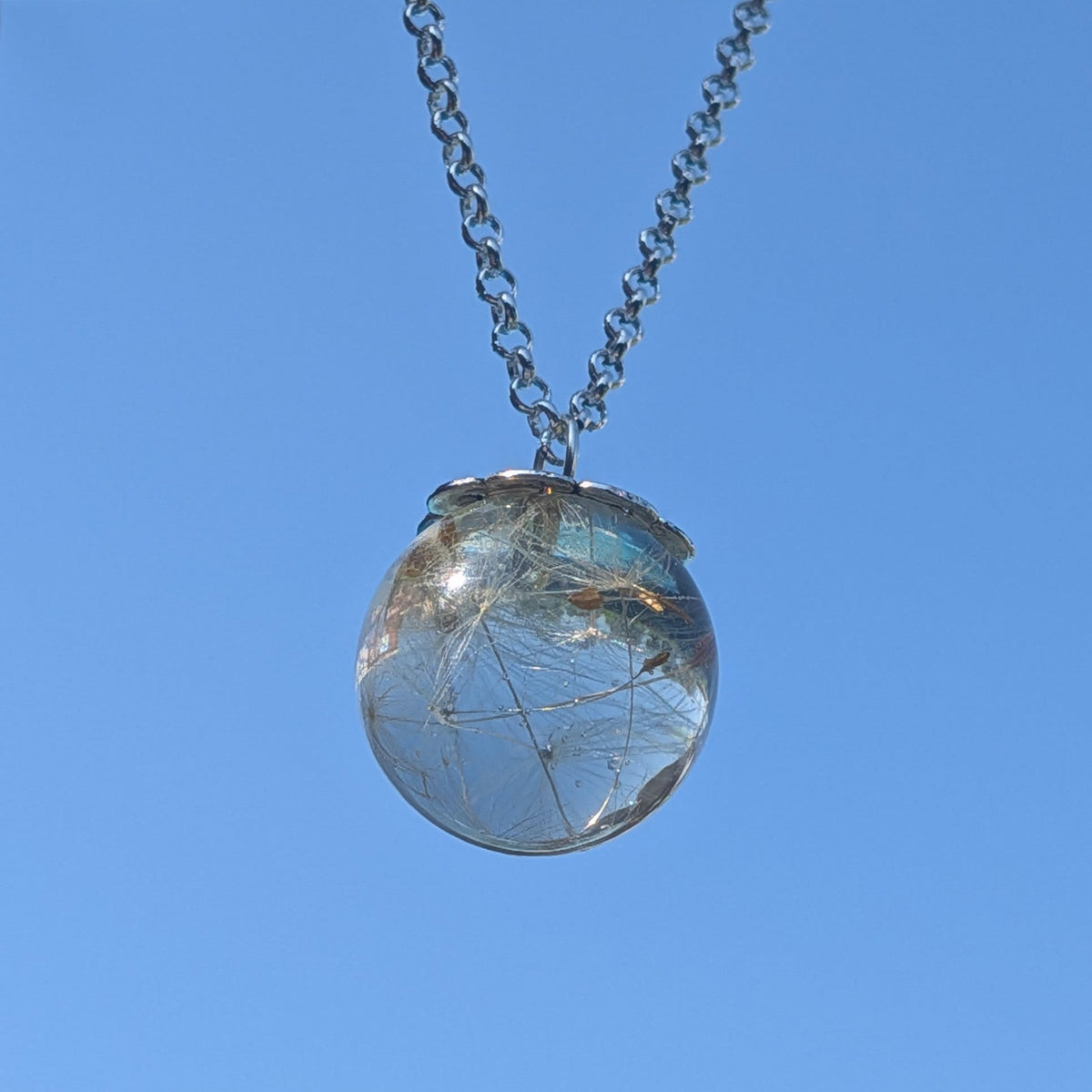 Clear resin orb pendant with whole dandelion seed heads against blue sky by EL-Creations