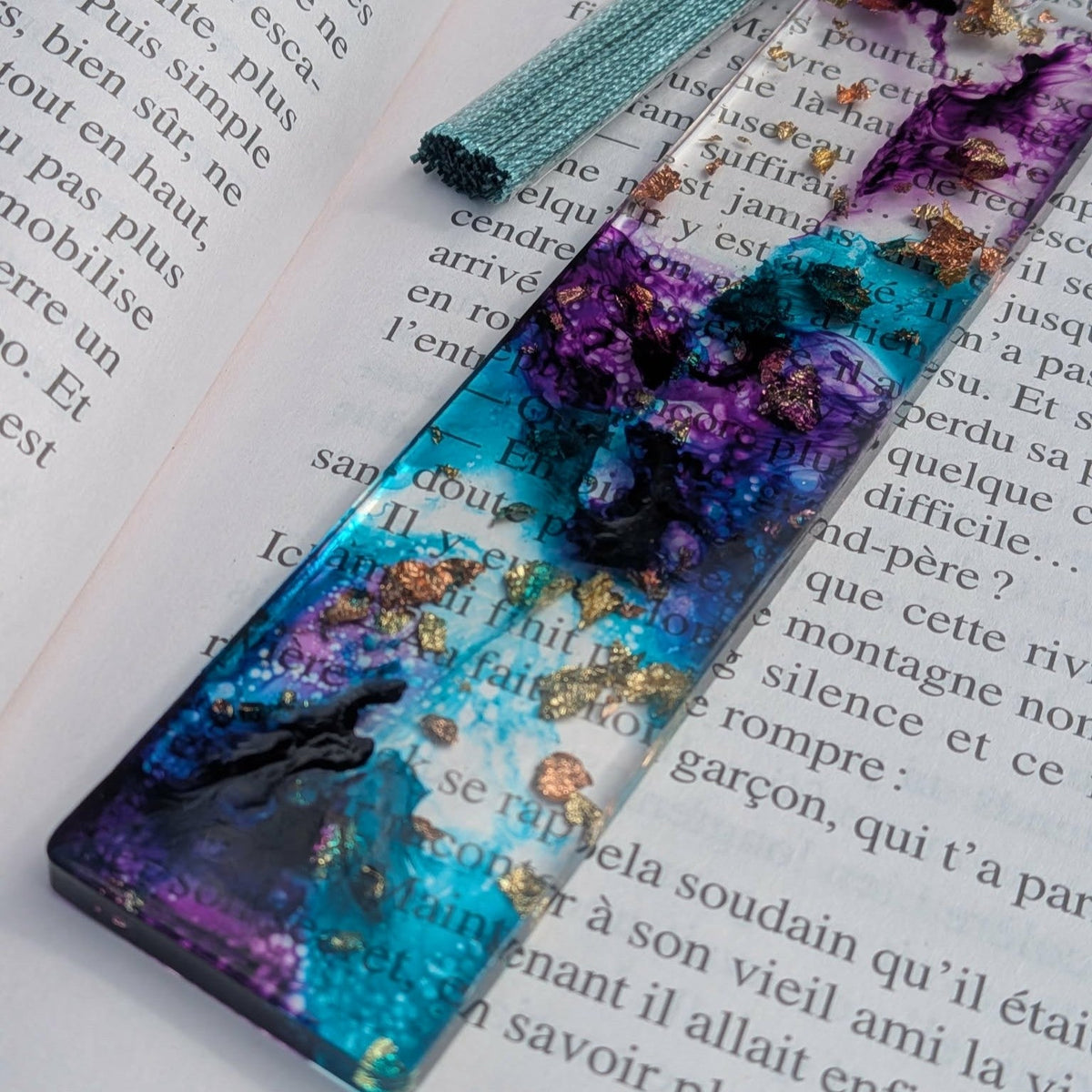 Cosmic tide resin bookmark with teal tassel keychain ring resting on open book – EL-Creations