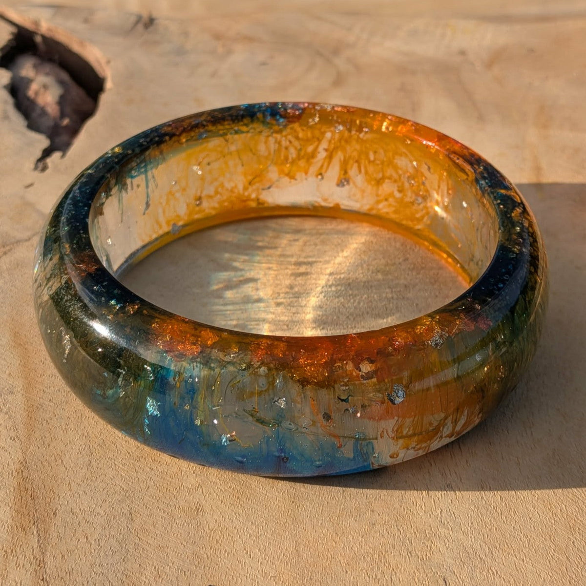 Side angle of amber tide resin bangle showing teal and orange layers on wood – EL-Creations