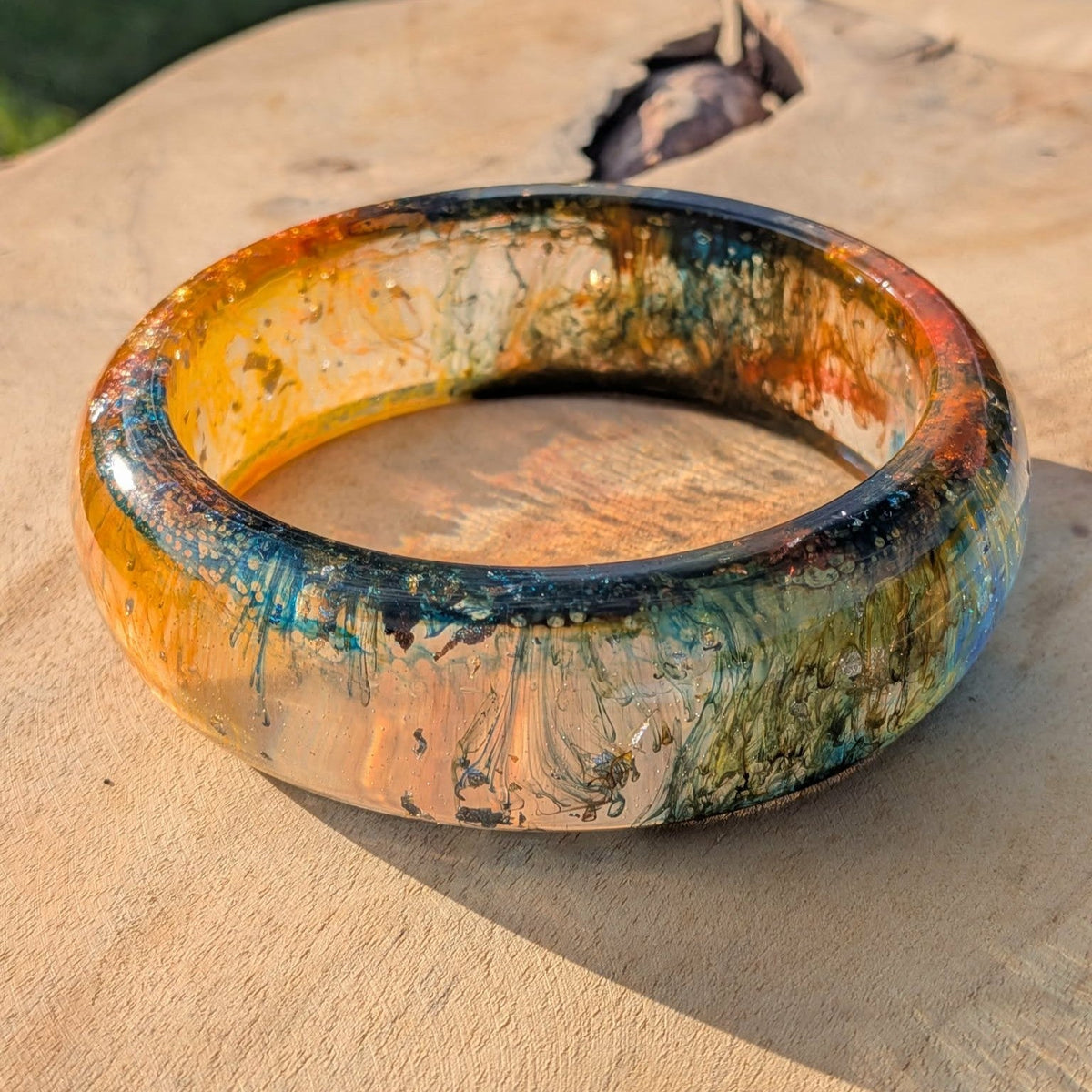 Three quarter view of amber orange resin bangle with teal gold detail on wooden surface – EL-Creations