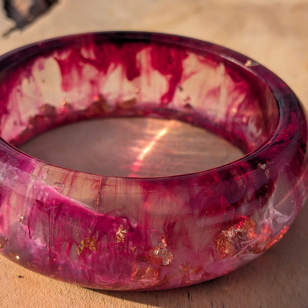 Wild berry resin bangle worn on wrist against brick wall showing burgundy and raspberry swirls – EL-Creations