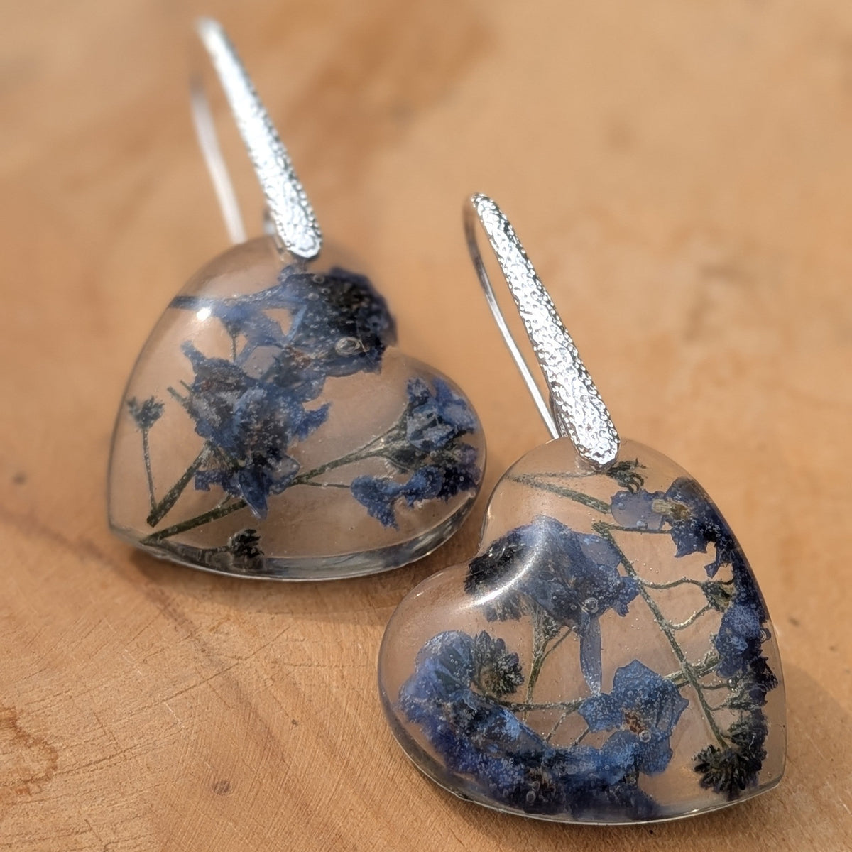 Pair of forget-me-not resin heart earrings on natural wood by EL-Creations