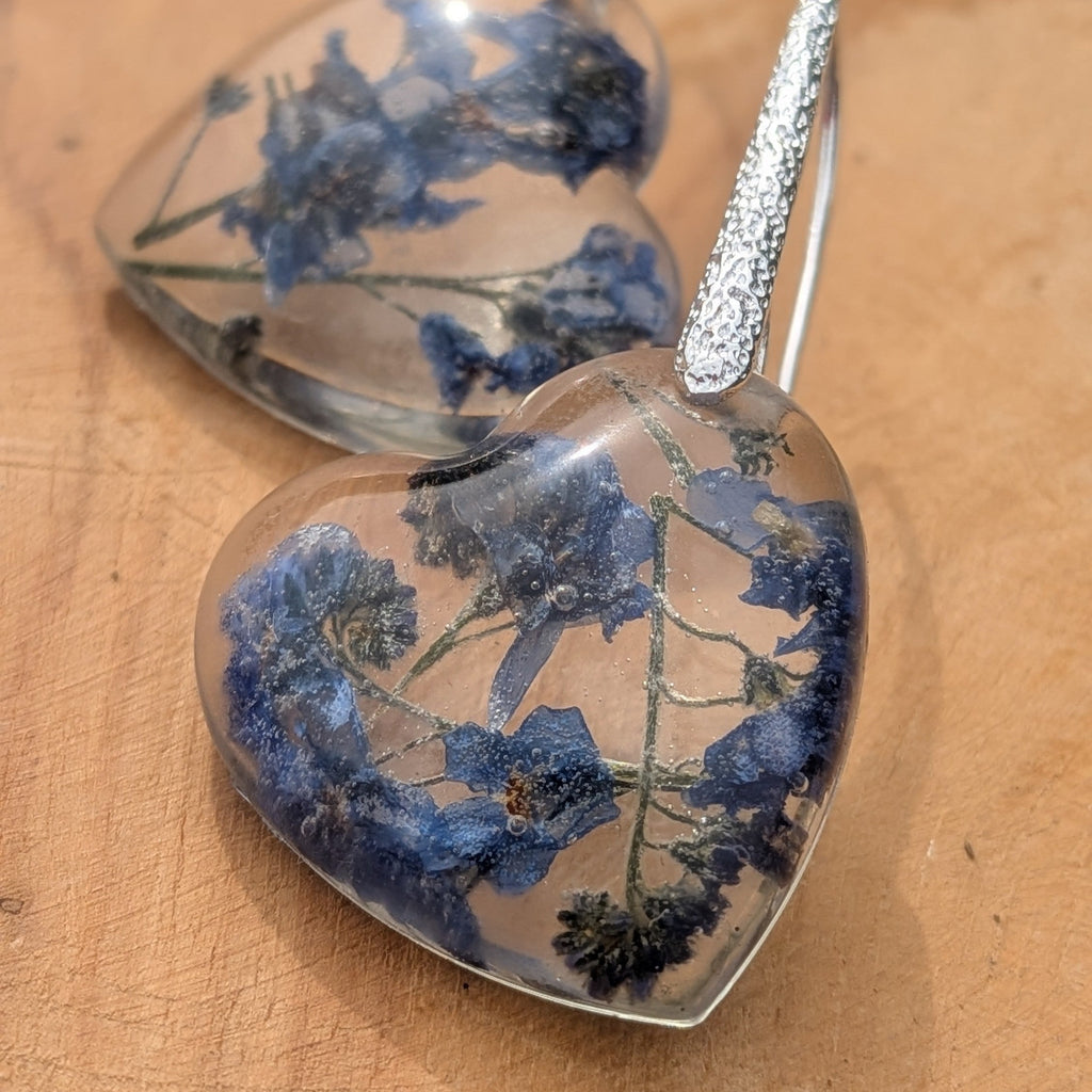 Close-up of preserved blue forget-me-not blossoms inside heart resin earrings by EL-Creations