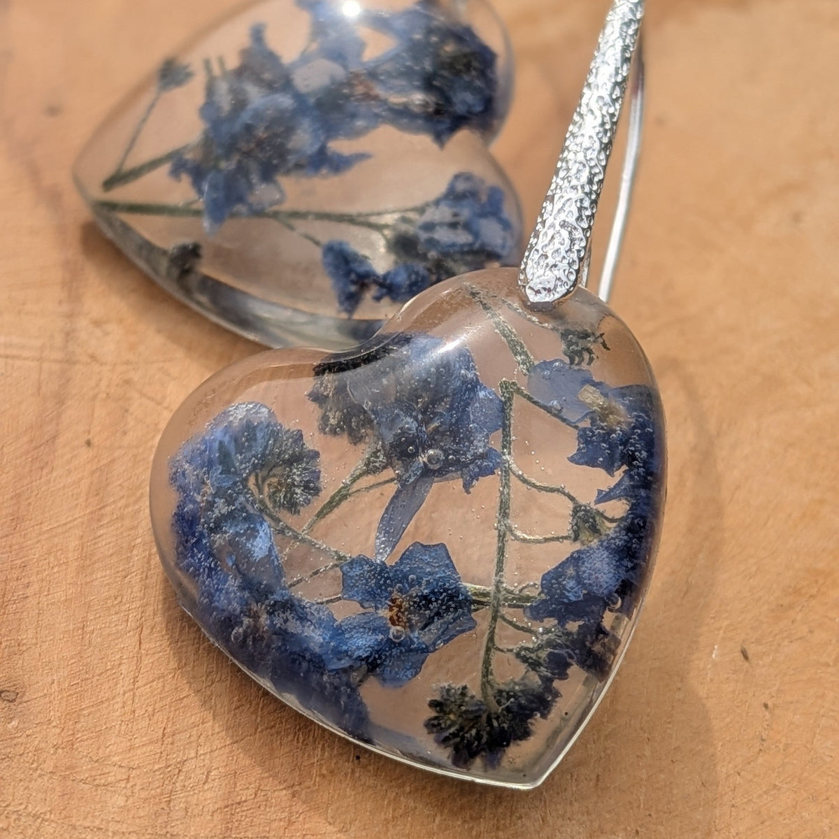 Close-up of preserved blue forget-me-not blossoms inside heart resin earrings by EL-Creations
