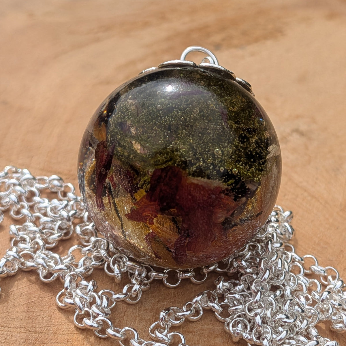 Handmade woodland moss resin sphere necklace resting on natural wood by EL-Creations