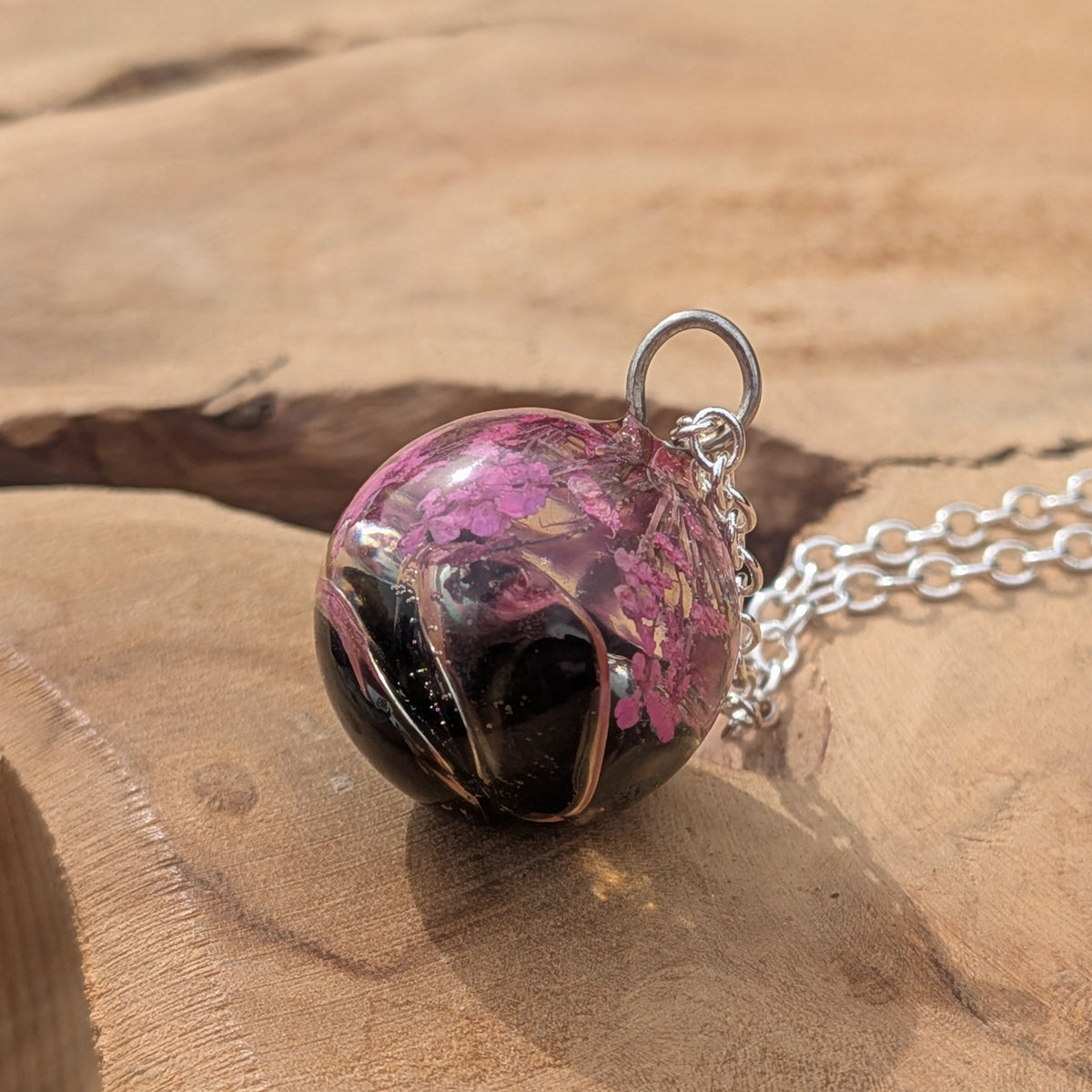 Handmade pink flower resin sphere necklace resting on natural wood by EL-Creations