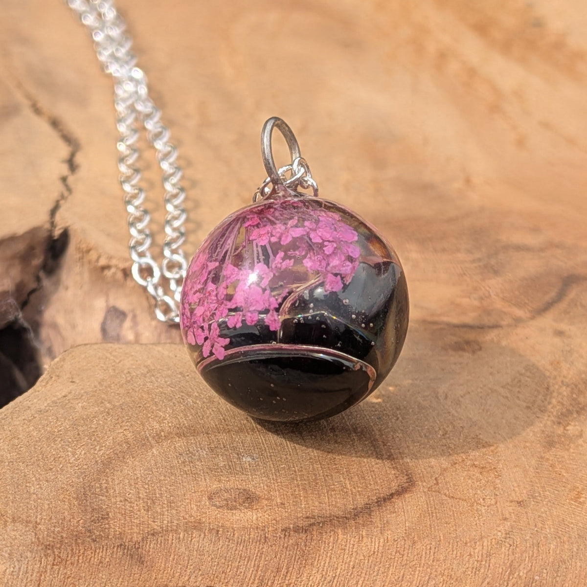 Close-up of preserved pink flowers inside black resin ball pendant by EL-Creations